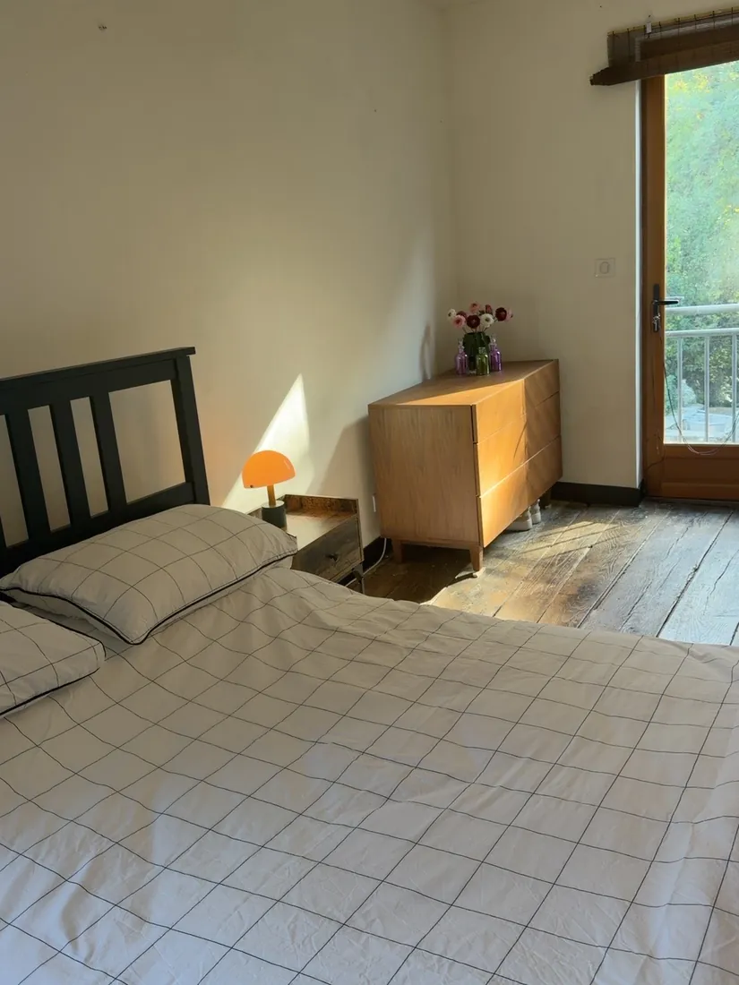 Bedroom Three from the other side: the dark wooden bed, a bedside lamp, a wooden chest of drawers and a glazed door onto greenery
